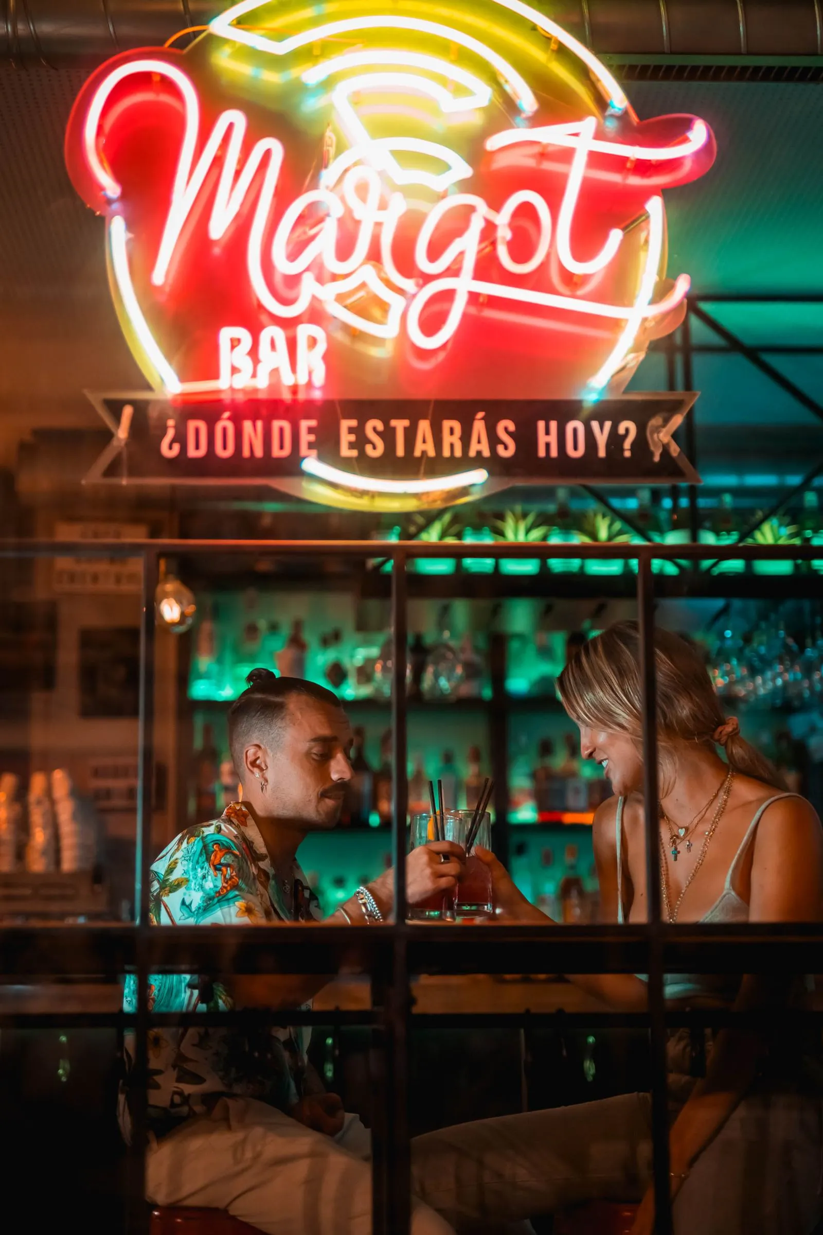 Pareja brindando con cócteles bajo el neón de Margot Bar